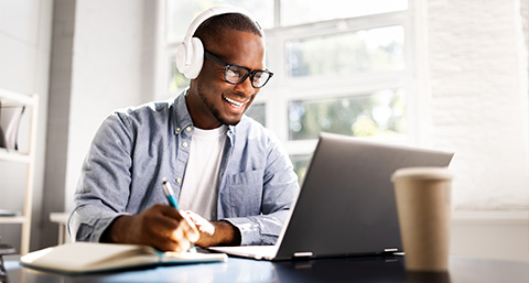 smiling man studying with laptop and headphones taking notes for online learning sessions 2 tips 2 strategies