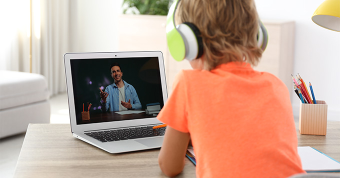 child attending online class on laptop wearing headphones engaged in video interaction with instructor